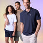 Three people smile while posing for a photo against a gradient background. The person on the left with curly hair wears a white t-shirt, the person in the middle with short hair sports a beige t-shirt, and the person on the right with short hair dons a Psycho Bunny MENS CLASSIC POLO - B6K001ARPC crafted from diamond-knit piqué fabric.