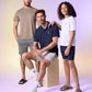 A group of three people posing for a photo in casual wear. One is standing in a beige shirt and shorts, another is seated wearing a Psycho Bunny MENS CLASSIC POLO - B6K001ARPC made from diamond-knit piqué fabric and light shorts, and the third is standing with a white Pima cotton polo and dark shorts, resting an arm on the seated person.