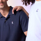 Close-up of two people wearing shirts, a navy blue men's classic polo shirt in diamond-knit piqué fabric (MENS CLASSIC POLO - B6K001ARPC by Psycho Bunny) and a white t-shirt, both featuring a small logo with a pink bunny head over crossed bones. One person has their hand resting on the other's shoulder.