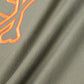 Close-up of a green fabric with an embroidered Bunny outline and abstract orange design. The fabric, reminiscent of a KIDS FLOYD GRAPHIC TEE - B0U338B2TS by Psycho Bunny, has soft folds and a smooth texture, accentuating the vibrant stitching which creates a dynamic contrast against the muted background.