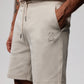 A person wearing MENS OUTLINE SWEATSHORT - B6R507X1CN with their left hand in the pocket. The double-faced jersey shorts, featuring a Psycho Bunny rabbit logo on the left leg, have a drawstring. The person has tattoos on their right arm and is standing against a plain background.