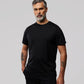 A man with gray hair and tattoos on his arms stands against a light gray background, wearing a black Psycho Bunny MENS OUTLINE TEE - B6U500ARPC and black pants. He looks directly at the camera with a serious expression.