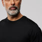 A close-up image of a mature man with gray hair and a beard wearing a plain black t-shirt from the Psycho Bunny OUTLINE collection, featuring a small rabbit logo on the chest, against a light gray background.