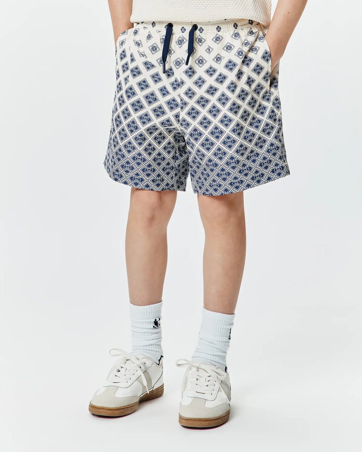 Kids Tobias Swim Trunk, cream with a navy blue all-over geometric pattern of the iconic Psycho Bunny skull logo, relaxed fit, smooth quick-dry fabric, and a navy drawstring. (1)