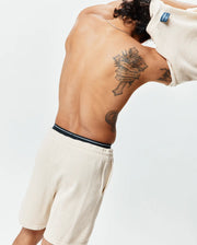 Cream Mens Devon Knit Short, a relaxed waffle knit short with a black and white striped waistband, paired with a matching cream waffle knit top featuring a blue Psycho Bunny tag at the back collar. (4)