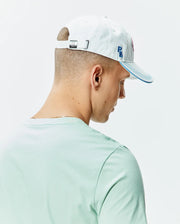 Pale blue Mens Ray Baseball Cap with blue brim stitching, embroidered blue PB initials, a pink Psycho Bunny skull logo, and a metal buckle with engraved bunny skull, paired with a light mint green jersey t-shirt. (3)