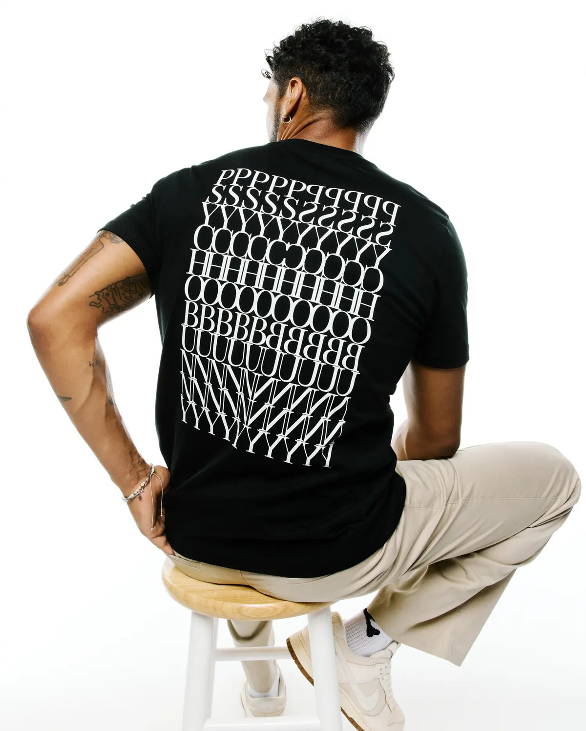 Mens Piers Pima Cotton Back Graphic Tee in black, featuring a large white stylized repeating letter graphic spelling PSYCHO BUNNY across the back, with a classic fit and smooth jersey texture. (1)