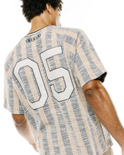 Mens Nathaniel Relaxed Raglan Tee in textured beige and navy vertical stripes, featuring a large white 05 graphic on the back and three small embroidered Psycho Bunny skull logos at the upper back neckline. (2)