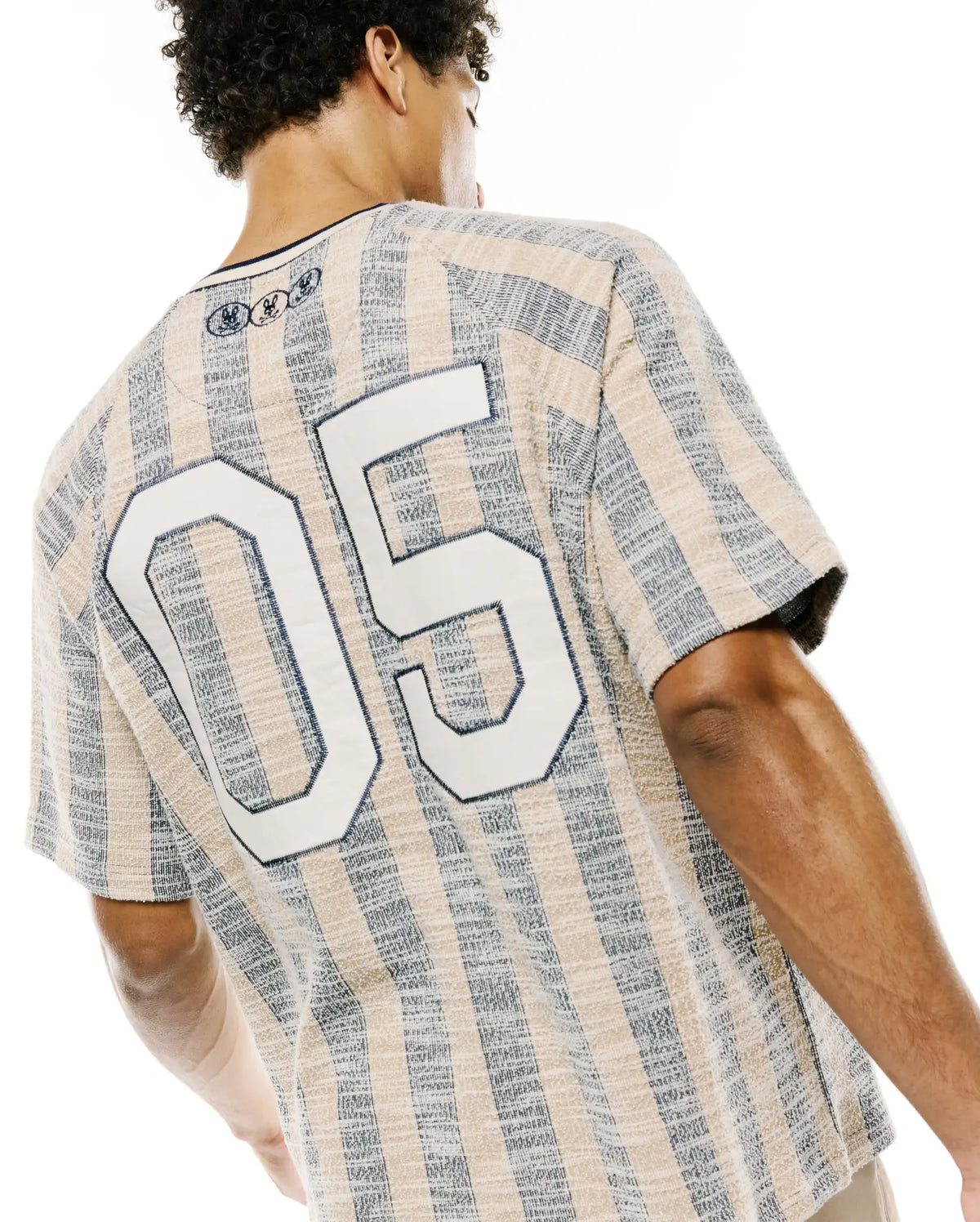 Mens Nathaniel Relaxed Raglan Tee in textured beige and navy vertical stripes, featuring a large white 05 graphic on the back and three small embroidered Psycho Bunny skull logos at the upper back neckline. (2)