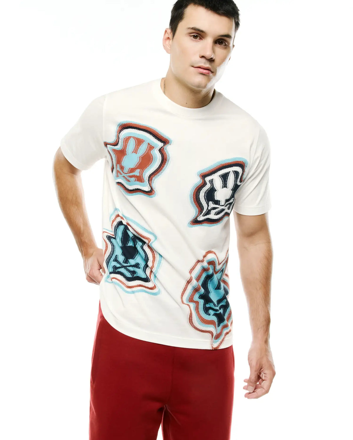 Men's Klaus Jacquard Tee, a cream classic fit jersey t-shirt featuring multiple large, distorted Psycho Bunny skull logos in red, blue, and black jacquard knit. (1)