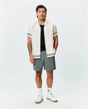 Mens Sunny Linen Shirt, cream, with black zigzag trim on sleeves and hem, paired with grey shorts featuring a small Psycho Bunny logo, white crew socks, and white sneakers. (4)