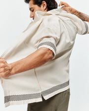 Mens Sunny Linen Shirt, an off-white relaxed-fit short-sleeve shirt with a black zigzag pattern on cuffs and hem, featuring a subtle orange side slit detail and breathable linen texture. (3)