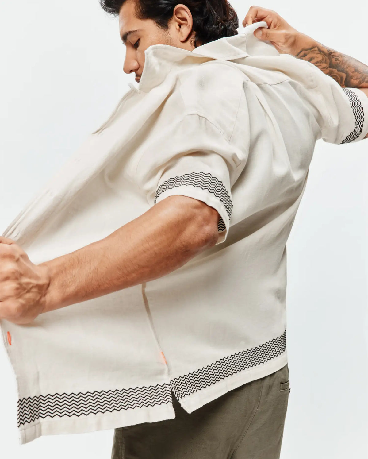 Mens Sunny Linen Shirt, an off-white relaxed-fit short-sleeve shirt with a black zigzag pattern on cuffs and hem, featuring a subtle orange side slit detail and breathable linen texture. (3)