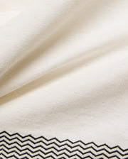 Mens Sunny Linen Shirt in crisp cream linen fabric, showcasing a refined black embroidered zigzag pattern with intricate stitching detail along the bottom hem. (6)