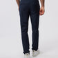 A man from the back wearing Psycho Bunny Men's Gable Regular Fit Sport Pants in navy blue stretch cotton-nylon textile and white sneakers on a plain background, focusing on his lower half.