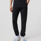 A person wearing black Psycho Bunny tech jogger pants and white with blue sneakers stands against a neutral background, focusing on the MENS CABRINI COMMUTER PANTS - B6P786U1CN.