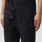 Close-up of a person wearing black MENS CABRINI COMMUTER PANTS with a drawstring waist and a small Psycho Bunny logo embroidered near the left pocket.