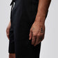 Close-up of a person's lower torso and arm, wearing black shorts with a Psycho Bunny logo. The person's arm shows several tattoos, including stars and a small figure.