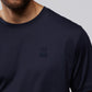 A man wearing a dark navy blue Psycho Bunny MENS OUTLINE TEE - B6U500ARPC, featuring an embroidered logo of a bunny head with crossbones underneath on the front. Made from soft Pima cotton, the image shows him from the shoulders to the upper chest against a plain gray background.