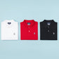 Three Psycho Bunny men's classic polo shirts (white, red, and black) neatly arranged side by side on a light blue background, each featuring a small Psycho Bunny logo on the left chest.