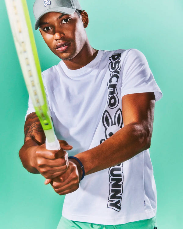 Mens Toby Wordmark Tee, a classic fit white jersey t-shirt featuring a bold vertical black Psycho Bunny wordmark graphic with the iconic bunny skull logo on the left side, and a small woven tag at the hem.