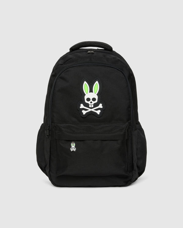 The KIDS BACKPACK - B0A175D200 by Psycho Bunny is a black backpack that features a large skull and crossbones emblem with green and white bunny ears on the front pocket. Below the emblem is a smaller patch with the same design. The bag includes adjustable shoulder straps, a laptop pocket, side pockets, and zippers.