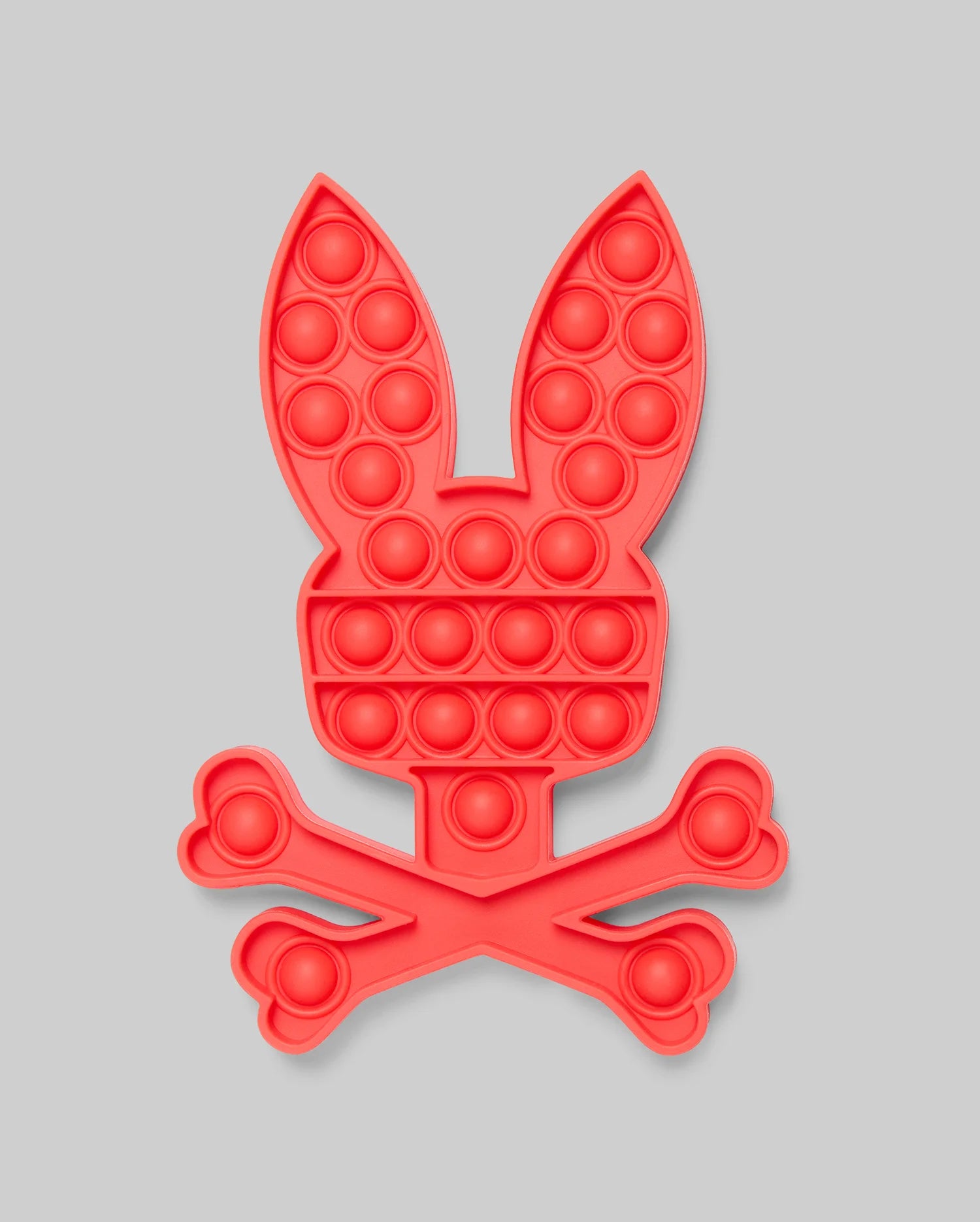 The PSYCHO BUNNY POP IT - B0A376E200 by Psycho Bunny features a red bunny head with long ears above crossed bones, resembling a fun skull-and-crossbones. Made from high-quality silicone for stress relief, set against a light gray background.