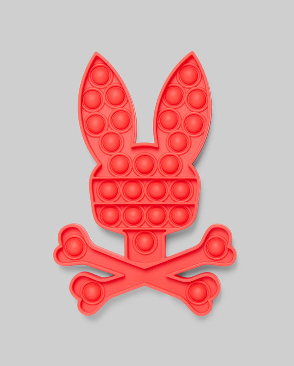 The PSYCHO BUNNY POP IT - B0A376E200 by Psycho Bunny features a red bunny head with long ears above crossed bones, resembling a fun skull-and-crossbones. Made from high-quality silicone for stress relief, set against a light gray background.