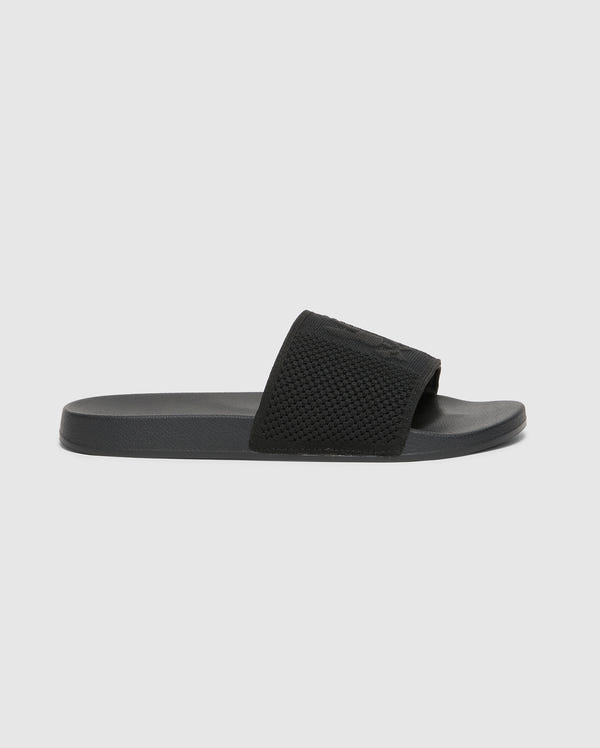 The Psycho Bunny KIDS KNIT SLIDES - B0A377F200 is a black slide sandal for kids, featuring a textured strap, flat sole, and molded footbed for comfort. It has a minimalist design without visible branding and is displayed on a plain white background.
