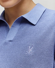 Close-up of a child wearing the Psycho Bunny KIDS LEETON KNIT POLO SHIRT (B0E562F200), featuring textured light blue cotton, a Johnny collar, and an embroidered bunny logo on the chest. Only the shirt, neck, and chin are visible.