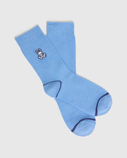 The KIDS 3 PACK FASHION DRESS SOCK by Psycho Bunny features a pair of light blue dress socks with dark blue toe and heel accents, crafted from Pima cotton. One sock has a small embroidered skull with bunny ears on a plain white background for a playful touch.
