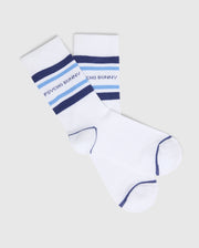 Psycho Bunny's KIDS 3 PACK FASHION DRESS SOCK - B0F504F200 features white athletic socks with blue stripes and "Psycho Bunny" text near the top, crafted from soft Pima cotton. They have navy trim on the toes, heel, and cuff and are displayed on a plain gray background.