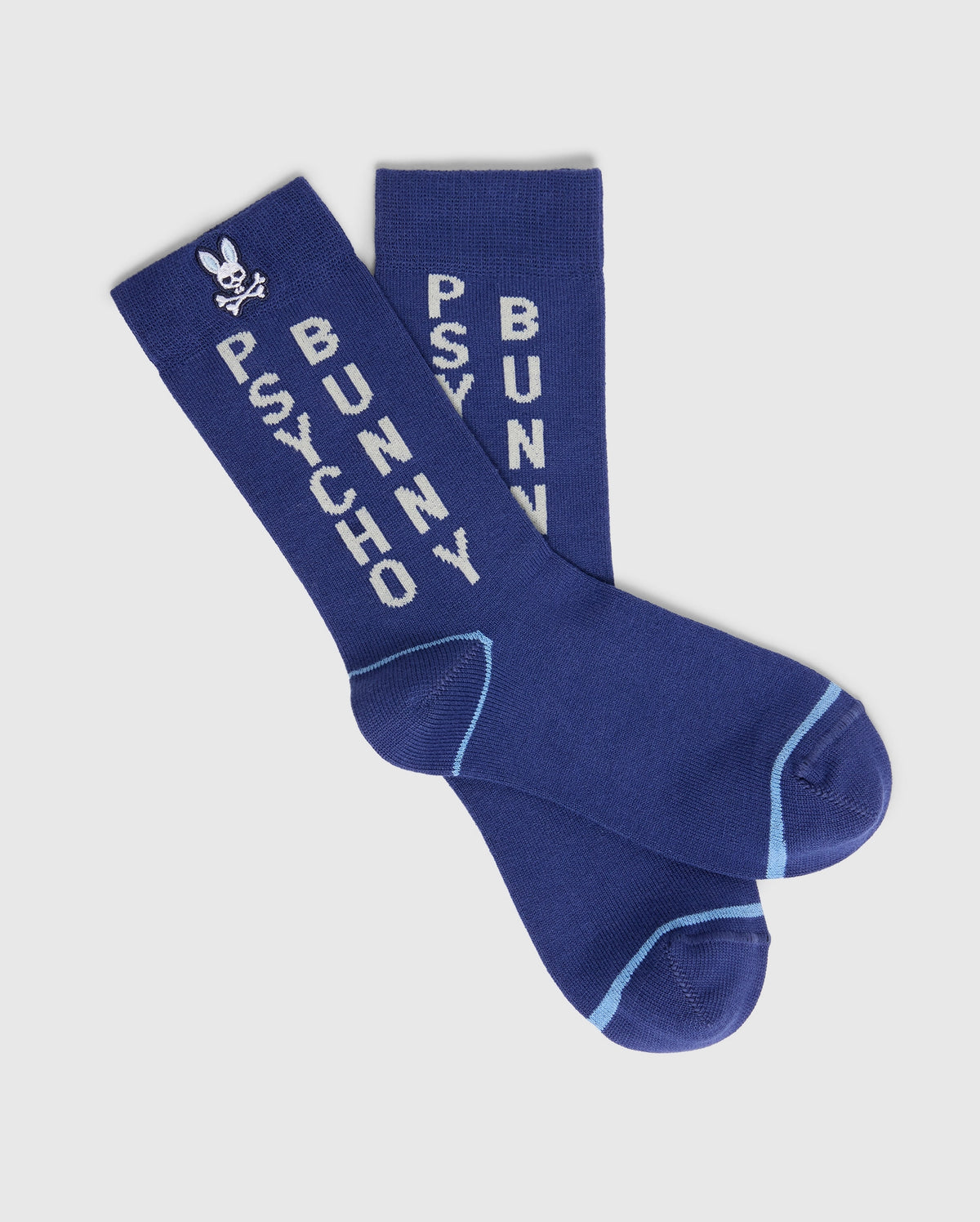 These blue KIDS 3 PACK FASHION DRESS SOCK - B0F504F200 by Psycho Bunny are made of soft Pima cotton and feature "PSYCHO BUNNY" in white text down each sock. A small white bunny with crossbones is at the top, and the toes and heels are accented in light blue.