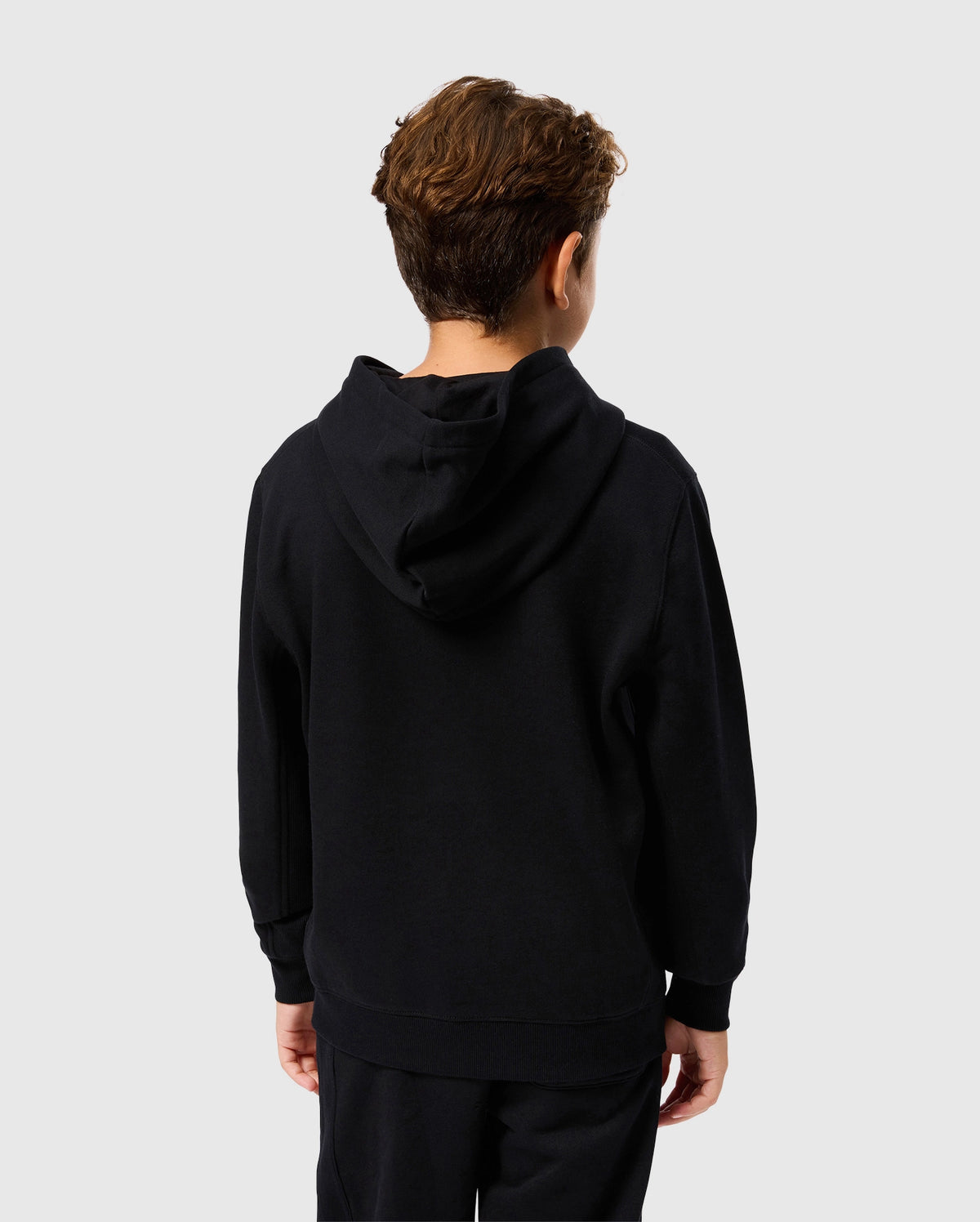 A young person faces away from the camera, wearing a Psycho Bunny KIDS LEVY FLEECE HOODIE - B0H859D200 along with matching pants. Made entirely from cotton for maximum comfort, this regular fit ensemble stands out against the simple, light-colored backdrop.