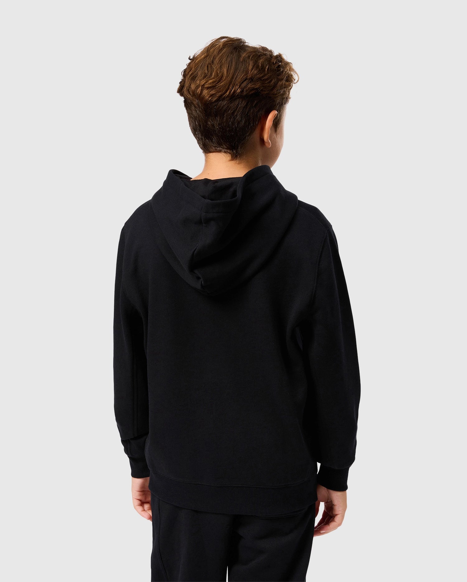 A young person faces away from the camera, wearing a Psycho Bunny KIDS LEVY FLEECE HOODIE - B0H859D200 along with matching pants. Made entirely from cotton for maximum comfort, this regular fit ensemble stands out against the simple, light-colored backdrop.