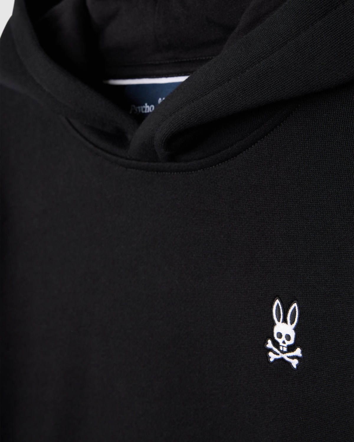 The KIDS LEVY FLEECE HOODIE - B0H859D200 by Psycho Bunny is crafted from 100% cotton and offers a regular fit. It boasts a black design accented by a small white logo on the chest, featuring a rabbit's head with crossed bones beneath it.