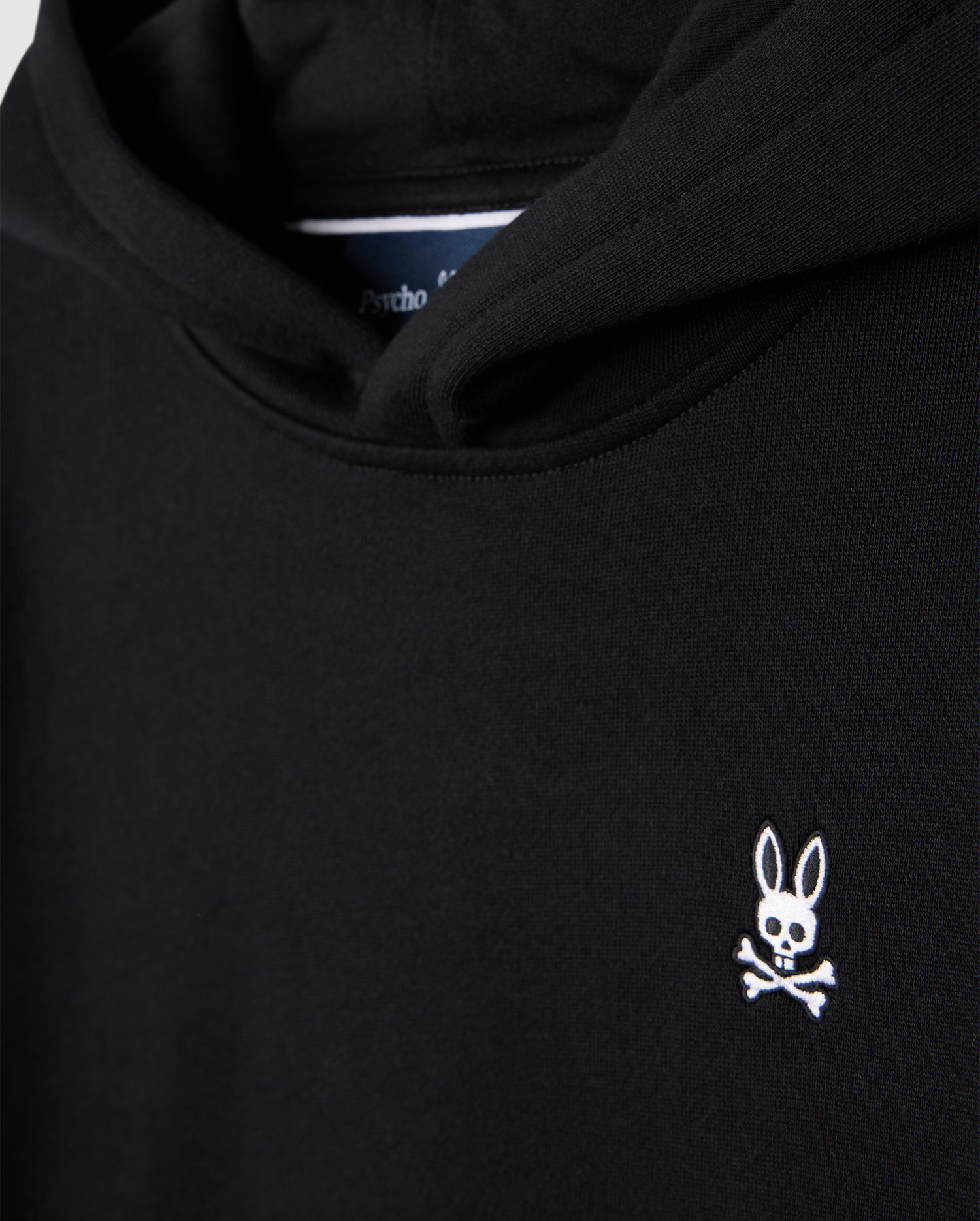 The KIDS LEVY FLEECE HOODIE - B0H859D200 by Psycho Bunny is crafted from 100% cotton and offers a regular fit. It boasts a black design accented by a small white logo on the chest, featuring a rabbit's head with crossed bones beneath it.