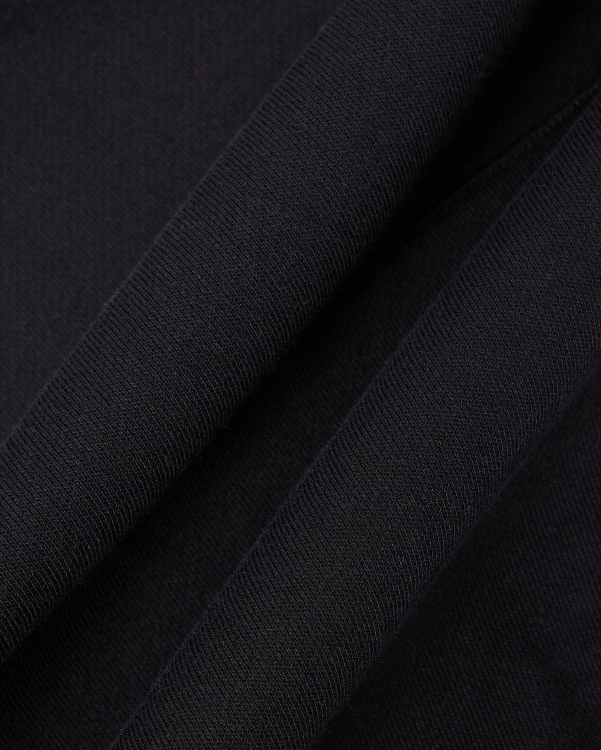 Close-up of black fabric from a Psycho Bunny KIDS LEVY FLEECE HOODIE (B0H859D200) showcases its soft, textured appearance. The 100% cotton material appears to be folded, creating subtle shadows and highlights that enhance the regular fit design.