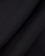 Close-up of black fabric from a Psycho Bunny KIDS LEVY FLEECE HOODIE (B0H859D200) showcases its soft, textured appearance. The 100% cotton material appears to be folded, creating subtle shadows and highlights that enhance the regular fit design.