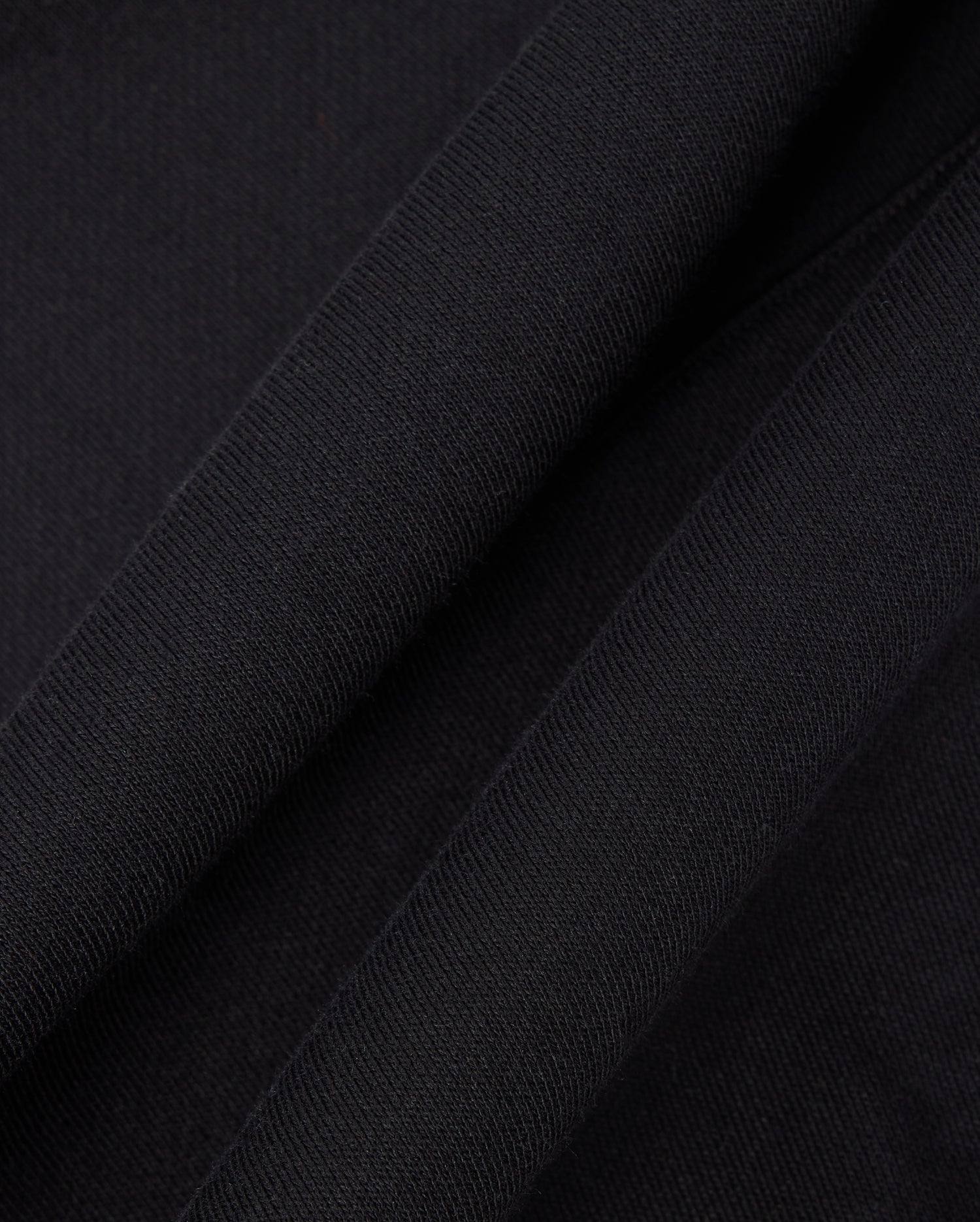 Close-up of black fabric from a Psycho Bunny KIDS LEVY FLEECE HOODIE (B0H859D200) showcases its soft, textured appearance. The 100% cotton material appears to be folded, creating subtle shadows and highlights that enhance the regular fit design.