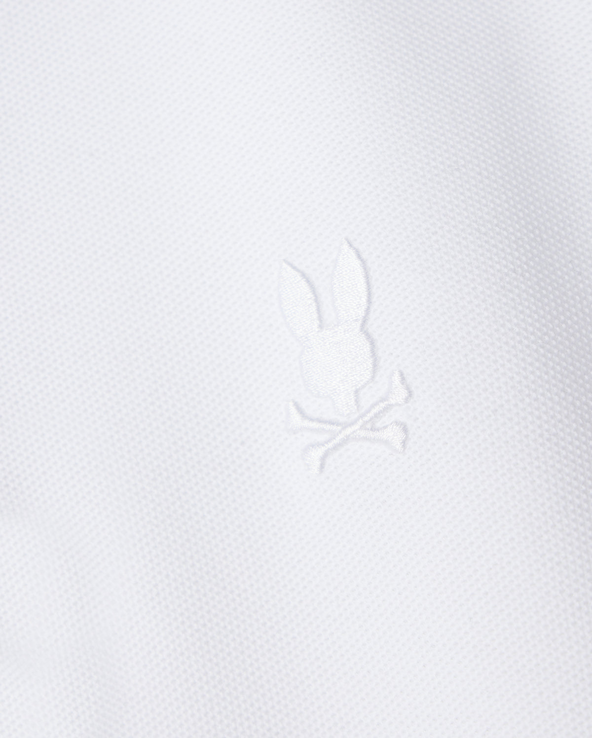 The Psycho Bunny Kids Classic Pique Polo Shirt (B0K021AR00) features a white fabric with a central embroidered Bunny motif above crossed bones, crafted in textured Pima cotton for a minimalist yet elegant design reminiscent of classic polo styles.