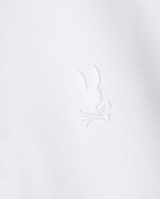The Psycho Bunny Kids Classic Pique Polo Shirt (B0K021AR00) features a white fabric with a central embroidered Bunny motif above crossed bones, crafted in textured Pima cotton for a minimalist yet elegant design reminiscent of classic polo styles.