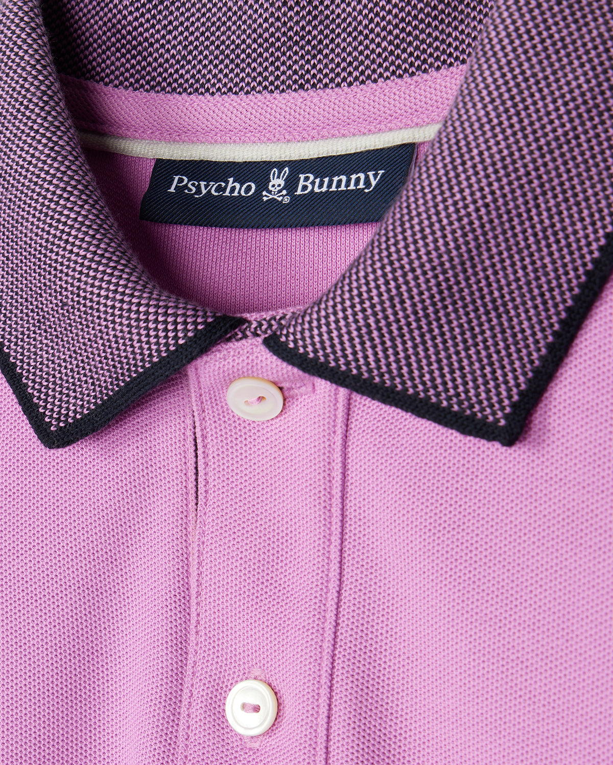 A close-up of a pink Psycho Bunny KIDS SOUTHPORT PIQUE POLO SHIRT - B0K263B200.