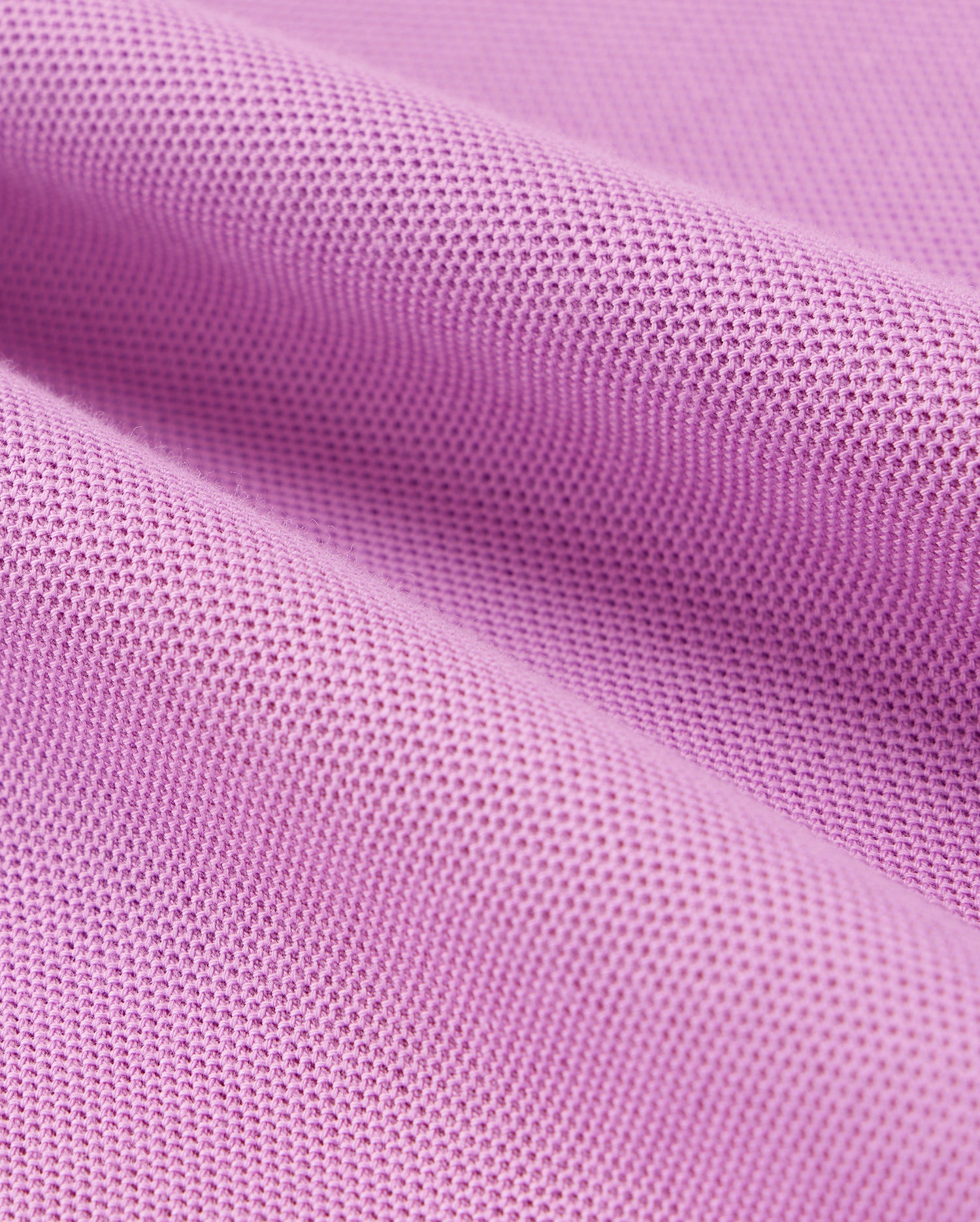 A close-up of a piece of pink Pima cotton fabric with a textured, waffle-like pattern. The fabric has several folds and appears soft, showcasing its detailed weave and structure. This is characteristic of the KIDS SOUTHPORT PIQUE POLO SHIRT - B0K263B200 by Psycho Bunny.