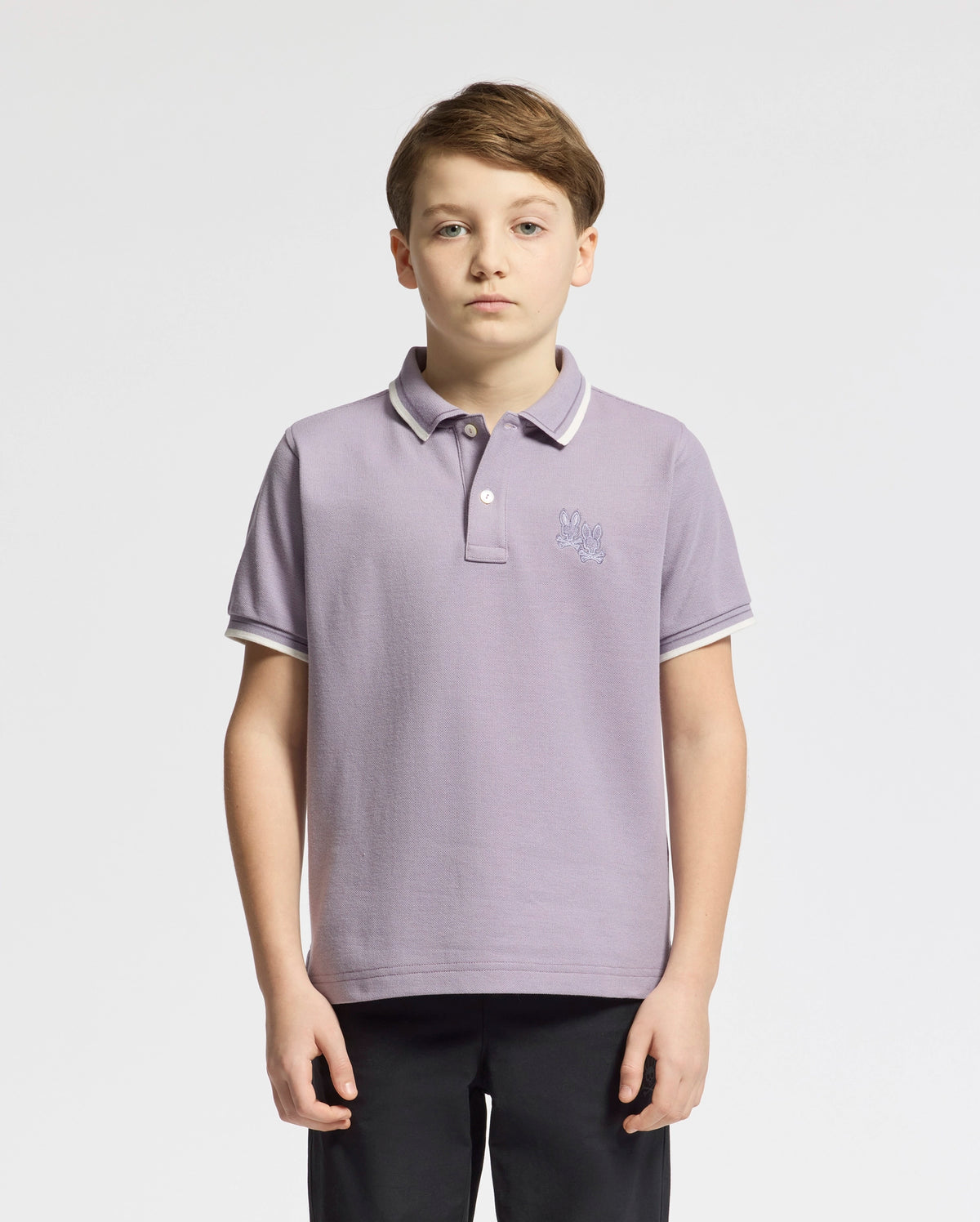 A boy with short brown hair wears a stylish Psycho Bunny Kids Elliot Pique Polo, color light purple, against a plain white background, looking at the camera with a neutral expression.