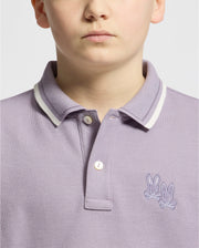 A fashionable individual models a Psycho Bunny KIDS ELLIOT PIQUE POLO in light purple crafted from soft Pima cotton featuring white trim and an embroidered design of two rabbits on the chest against a plain off-white background.