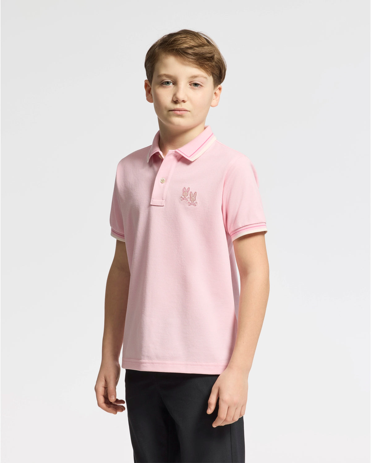 A young boy with short hair looks straight at the camera against a plain white background, wearing a Psycho Bunny KIDS ELLIOT PIQUE POLO - B0K505F200, made from soft Pima cotton and featuring a small embroidered logo on the chest.
