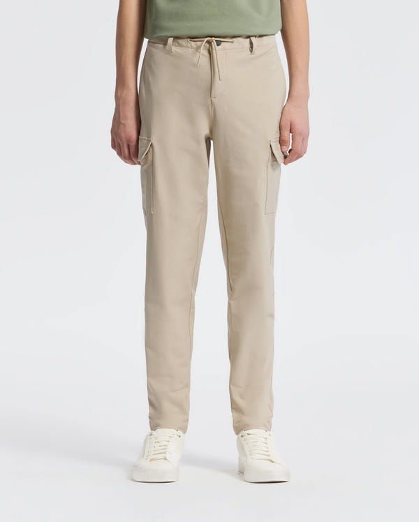A person in Psycho Bunny's KIDS GREEN VALLEY CARGO PANT (B0P199E200) and white sneakers stands against a plain white backdrop, hands down by their sides, with a hint of a green shirt showing.