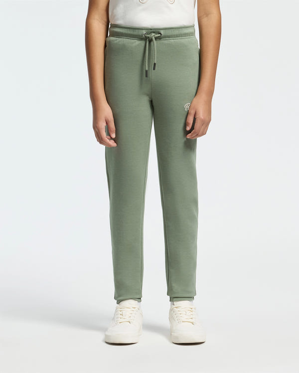 A person wearing the KIDS DESERT EMBROIDERED SWEATPANT by Psycho Bunny, crafted from a soft stretch jersey, alongside a white shirt and sneakers, stands against a plain light background.