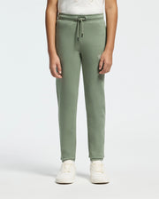 A person wearing the KIDS DESERT EMBROIDERED SWEATPANT by Psycho Bunny, crafted from a soft stretch jersey, alongside a white shirt and sneakers, stands against a plain light background.